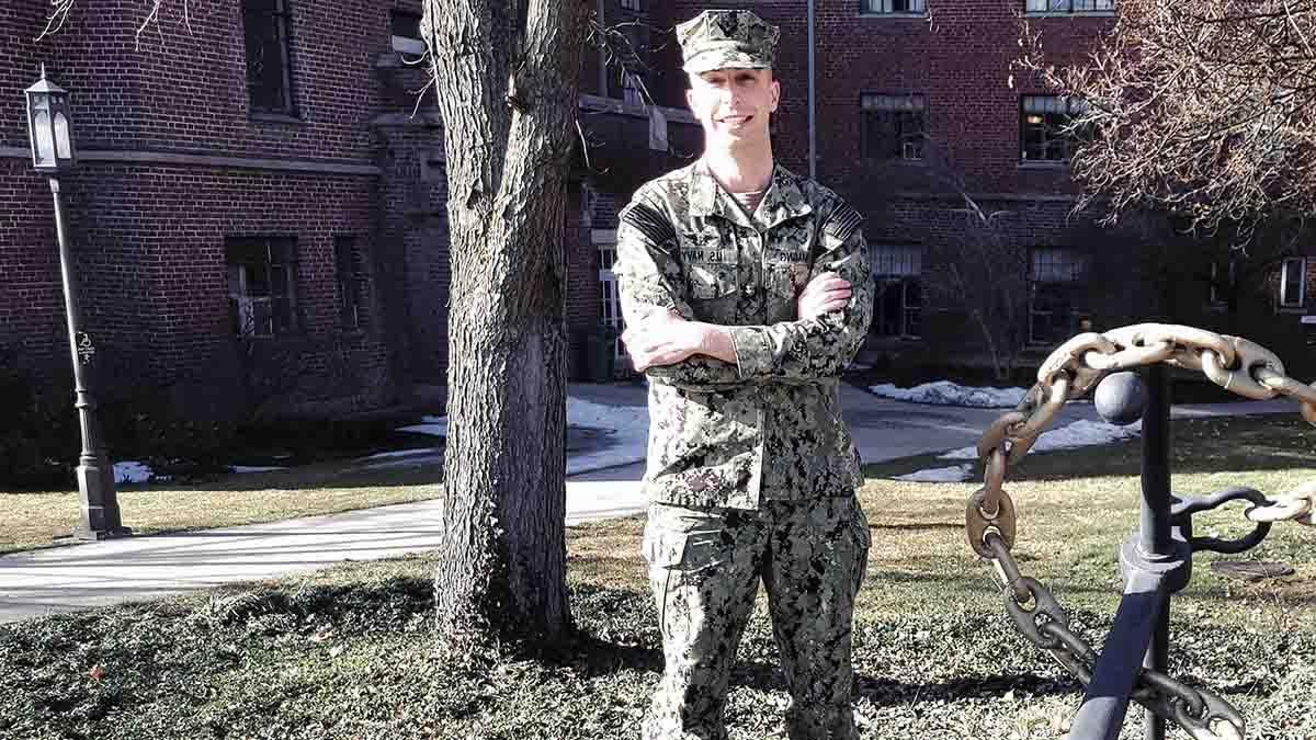 Man in camouflage fatigues stands near boat anchor.