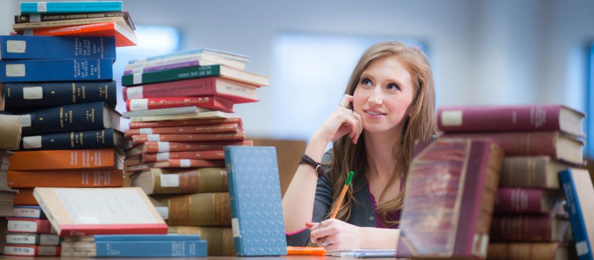 A student surrounded by books in the library.