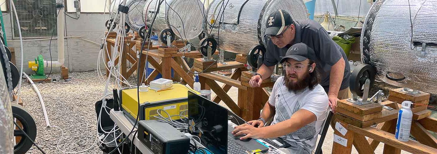 Two men look at a computer in a room with dairy manure composters.