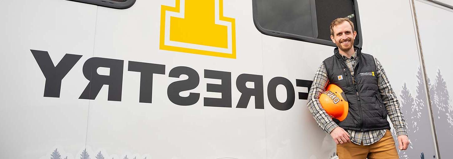 Man holding hard hat st和s in front of an enclosed trailer.